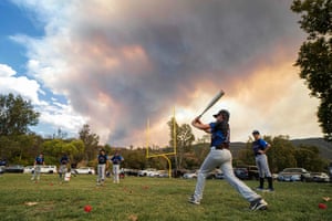 Little League players warm up before a game as brush burns in the background near Dehesa, in San Diego