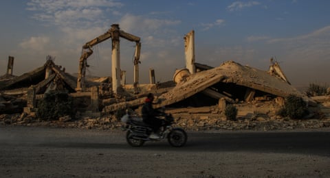 A person on motorbike rides past the remains of destroyed buildings in Daraya, Syria