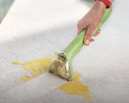 close-up of person cleaning yellow stain from upholstery with green device