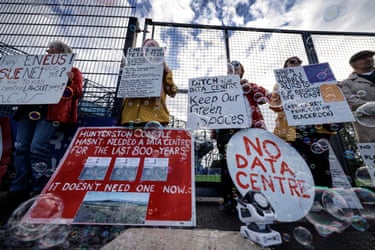 People stand in front of a gate holding handmade signs protesting against datacentre plans