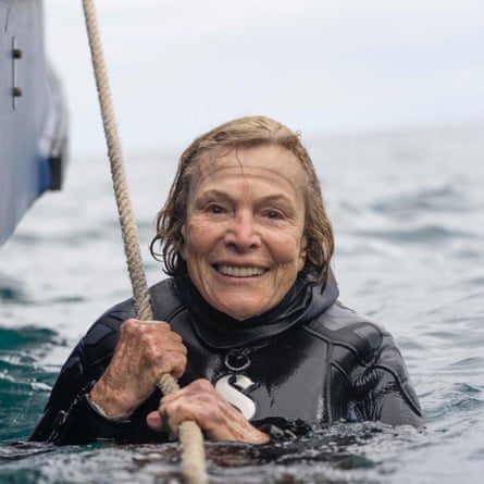 A woman wearing a diving suit in the sea, holding on to rope next to a boat.