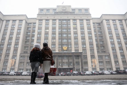 Two women stand facing away from camera, looking up at State Duma building in the snow