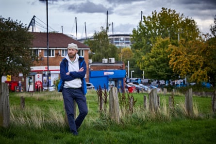 Matthew Stallard, foodbank chair, stands arm-crossed in a field with a stadium visible behind