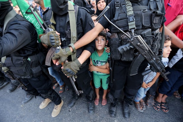 Palestinian boys stand next to Hamas militants as they take part in a military show