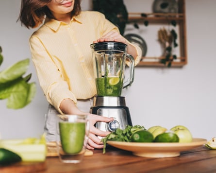 Close up of young woman with blender and green vegetables making detox shake or smoothie at home