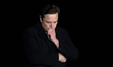 Musk photographed against a black background, with his chin in his hand, looking down