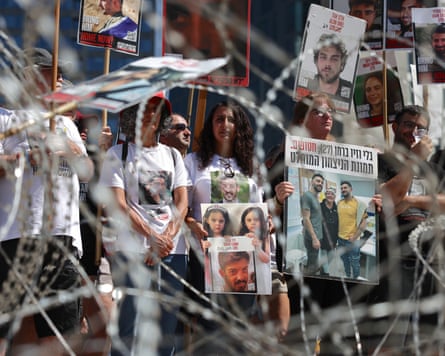 People stand behind coils of razor wire hold placards displaying pictures of hostages held in Gaza.