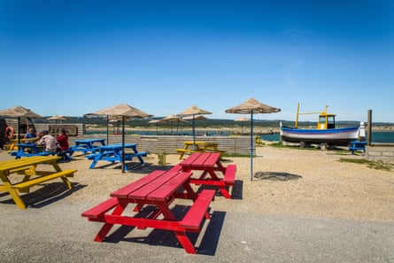 Red yellow and blue tables and benches on a sunny beach with a boat