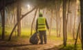 A man in a hi-vis vest seen from behind as he picks rubbish amid some trees