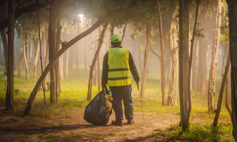 Một người đàn ông mặc áo vest nhìn từ phía sau đang nhặt rác giữa những tán cây
