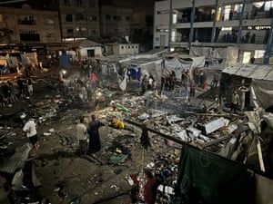 A night shot of people standing amid the ruins of burned out tents