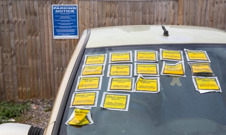 Parked car with multiple parking charge notice stickers on the windscreen.