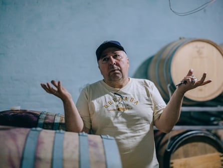 Mykhailo Molchanov holds out his hands as he stands behind a barrel, with barrels stacked along the wall behind him