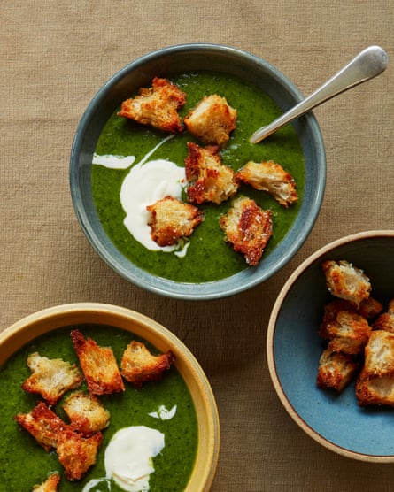 Overhead shot of a green vegetable soup in a bowl, with a dollop of creme fraiche and large croutons