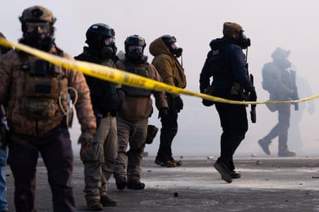 masked federal agents in tactical gear stand in a cloud of tear gas