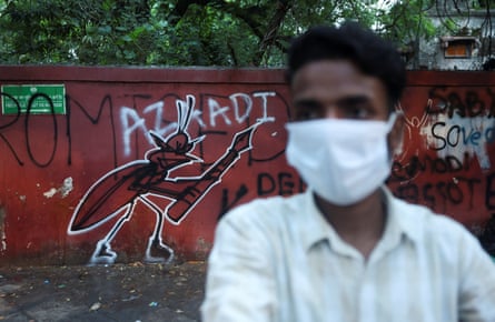 A supporter of India’s Cockroach Janata party (CJP) stands next to a graffiti of a cockroach holding a pen at the ongoing protest site at Jantar Mantar in Delhi.