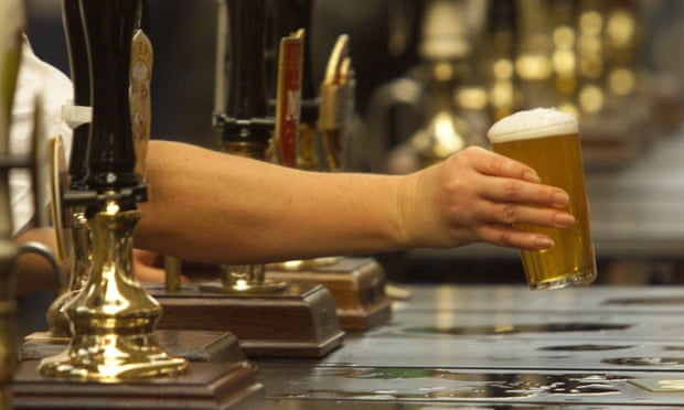 A hand holding a pint of beer in a pub