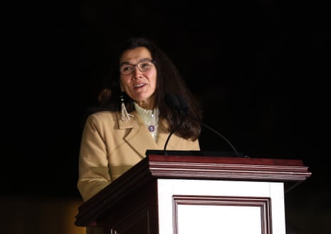 Mary Peltola speaks at a podium with microphones, illuminated against a dark background.