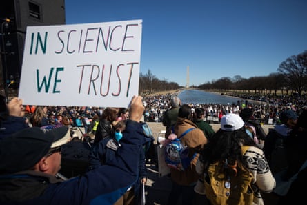 a person holds a sign that reads ‘in science we trust’