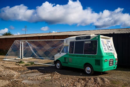 An ice cream van next to a football goal on a muddy patch of ground