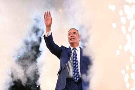 Farage waves to the crowd while on stage in front of several columns of pyrotechnic smoke