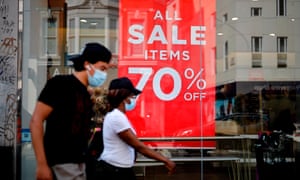 Shoppers wearing a face mask or covering due to the COVID-19 pandemic, walk past sales signs in the window of a shop in London last August