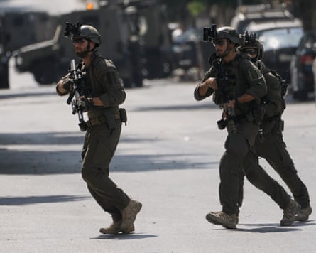 Soldiers carrying weapons run across a road
