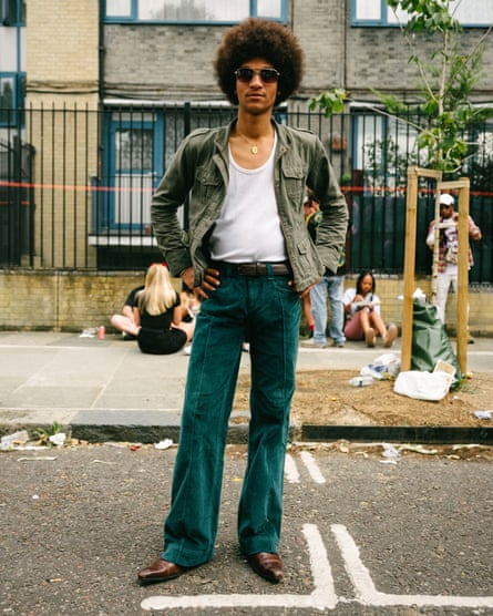 Djily poses in a jacket, cords, sunglasses and smart shoes