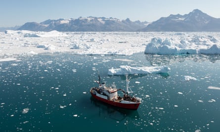 A research vessel on a green sea near an ice sheet, surrounded by chunks of sea ice.