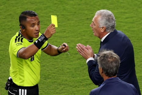 Referee Ivan Barton issues a yellow card to Carlos Gonzalez (not pictured) of Paraguay, as Gustavo Alfaro, Head Coach of Paraguay, reacts.