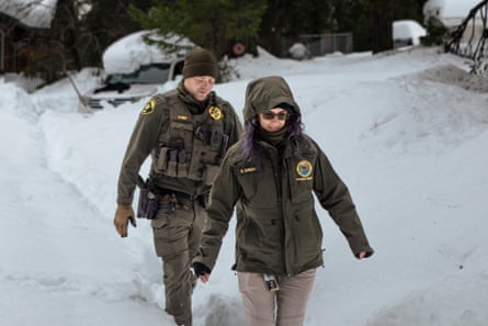 A man and woman wearing cold-weather gear walk carefully through the snow.