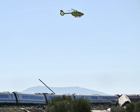 A yellow rescue helicopter flies over derailed train carriages after a crash near Toledo, Spain