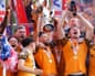 Hull players celebrate together, hoisting the trophy and bottles above their heads with medals around their necks