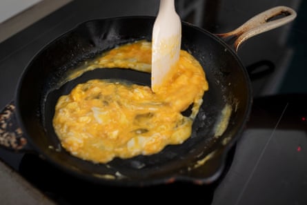 Le Creuset cast iron pan with scrambled eggs cooking and being stirred by a silicone spatula