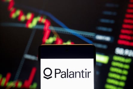 A Palantir logo on a smartphone against a backdrop of glowing stock price charts.