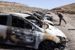 A man looks at a vehicle in a row of burned cars