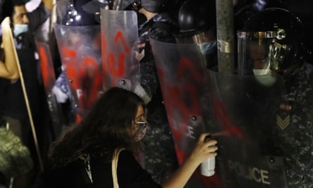 A supporter of relatives of people who were killed in last year’s massive blast at Beirut’s seaport, left, sprays the word “Revolution” in Arabic on the shields of riot police.