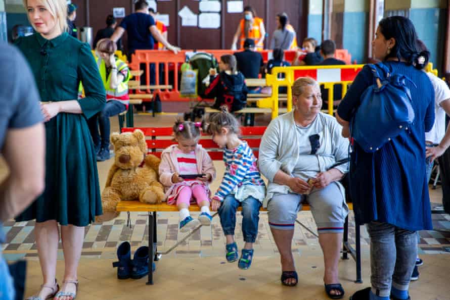 Two small children are sitting on a bench with a teddy bear next to a tired looking older woman