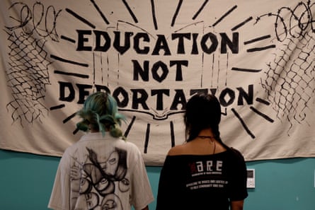 two sisters hold hands and face a banner that reads ‘education not deportation’