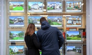 A couple look at houses for sale in an estate agents window