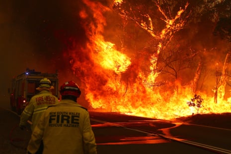Firefighters run to their truck as a large blaze burns in trees nearby in the night