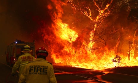 Fire and rescue personal run to move their truck as a bushfire burns next to a major road and homes on the outskirts of the town of Bilpin in Sydney, Australia, December 2019. 