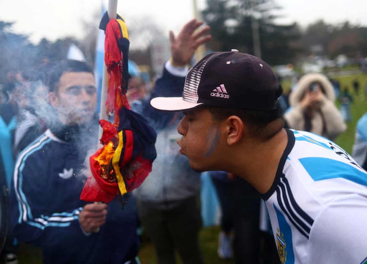 A man wearing a replica Argentina shirt and baseball cap blows on a burning Spain shirt to try to fan its flames