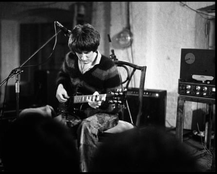 Black and white photograph of a young man strumming on a guitar next to recording equipment