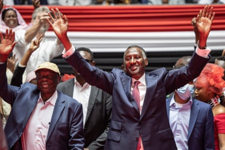 Abdul Rahim Dagalo, wearing a suit and tie, walks at the head of a crowd with his hands raised in greeting.