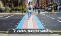 A woman walks along a pedestrian crossing with trans flag