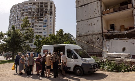 Local residents receive meals delivered by volunteers in front of a damaged residential building in Chernihiv.