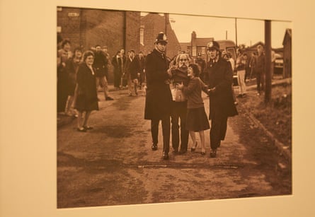 A photograph showing two police officers leading away an elderly man as a distressed woman clings to him