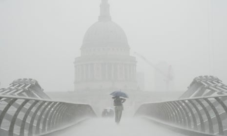Person shelters under an umbrella in heavy rain with St Paul's Cathedral in the background