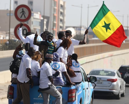 Supporters of opposition presidential candidates riding in the back of a pickup truck, waving a Senegalese flag.